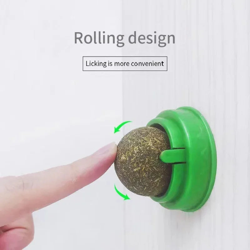 "Green rolling ball treat dispenser mounted on a wall with a human finger rotating it; enhances pet feeding convenience with interactive design."